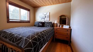 Quarto com cama, mesa de cabeceira, espelho e janela com persianas.
