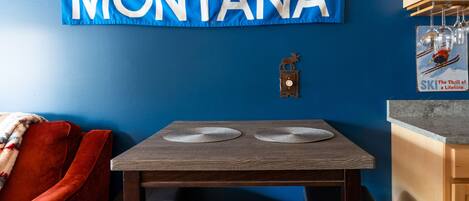 A dining area with a wooden table and chairs, a blue wall with a 'Big Sky Montana' banner, and a red couch.
