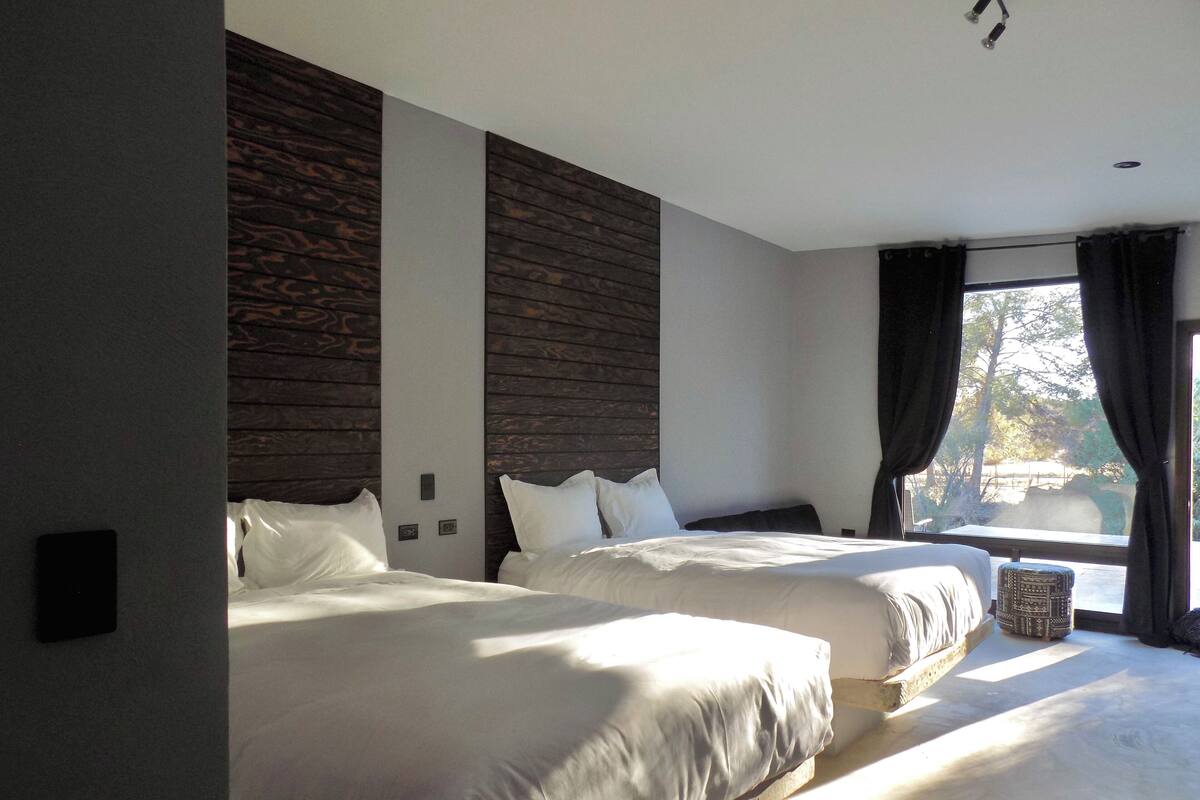 Ein modernes Hotelzimmer mit zwei Betten, einem großen Fenster mit Vorhängen und Blick ins Freie.