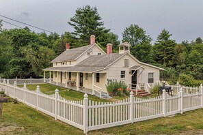Ein zweistöckiges Haus mit Veranda, umzäunter Garten und Schornstein.