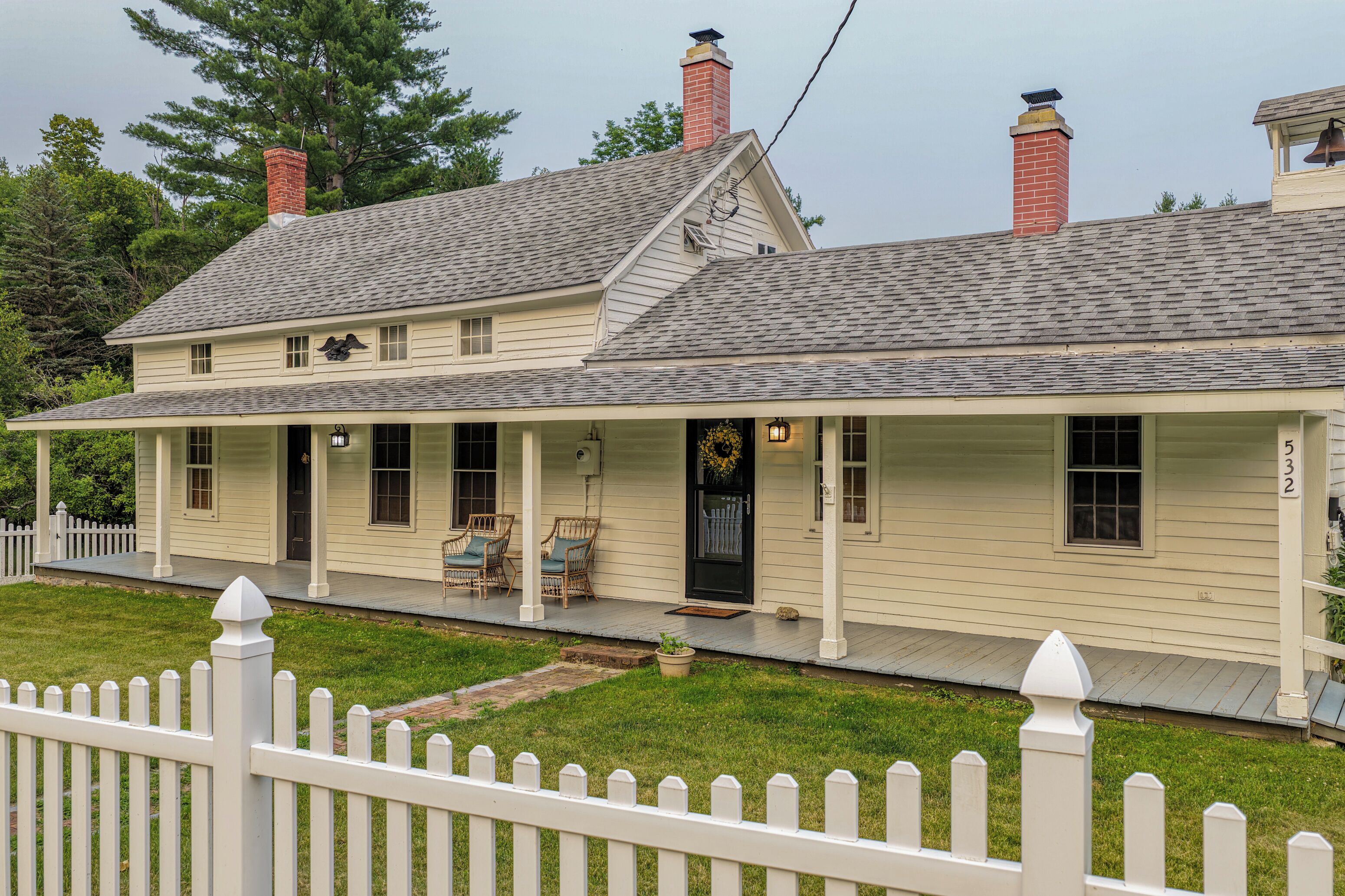 A two-story house with a covered porch, a front door with a wreath, and a white picket fence.