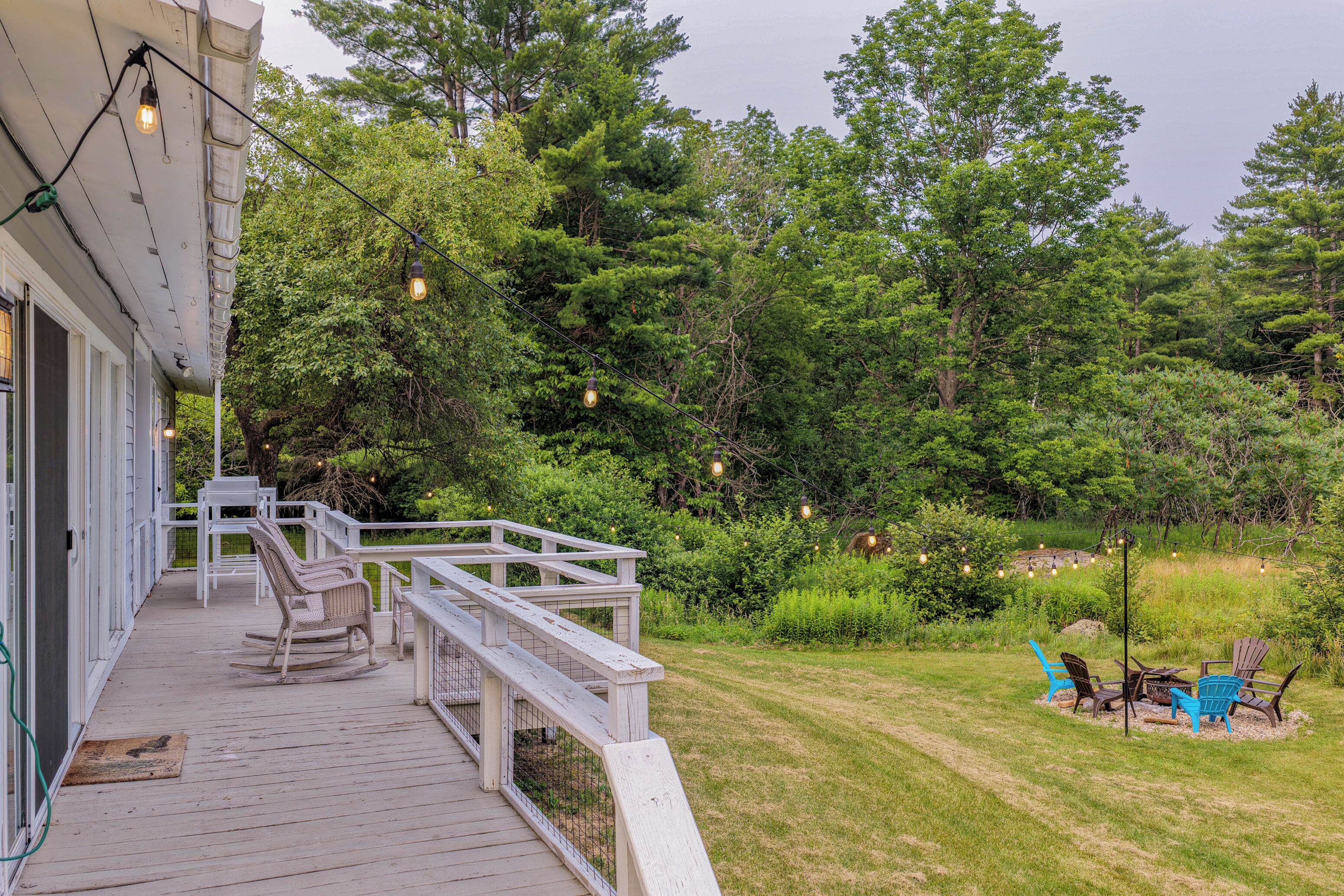 Une terrasse en bois, agréée de mobilier d’extérieur, entourée d’un paysage verdoyant et luxuriant et d’arbres.