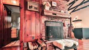 Un interior rústico con chimenea de ladrillo, leña y un banco blanco mullido.