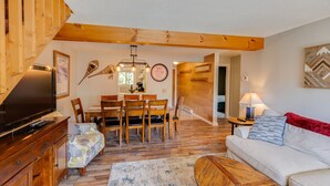 A cozy living room with a wooden dining table, a sofa, and a TV. - Loon Mountain Condo- Walk to Main Street! (Lincoln)
