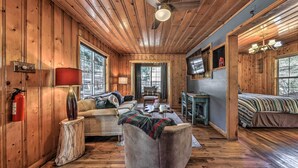 Ein gemütliches Cabin-Interieur mit Holzwänden, einem Deckenventilator, einer Couch, einem Bett und einem kleinen Tisch.