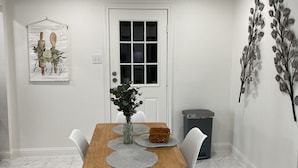 A dining area with a wooden table, white chairs, a vase with flowers, and a decorative wall piece.