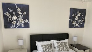 A neatly arranged bedroom with a large bed, two nightstands, and two wall-mounted paintings of birds and flowers.