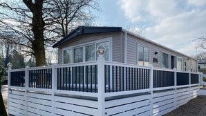 Een stacaravan met een witte buitenkant, een zwart dak en een wit terras met zwarte reling.