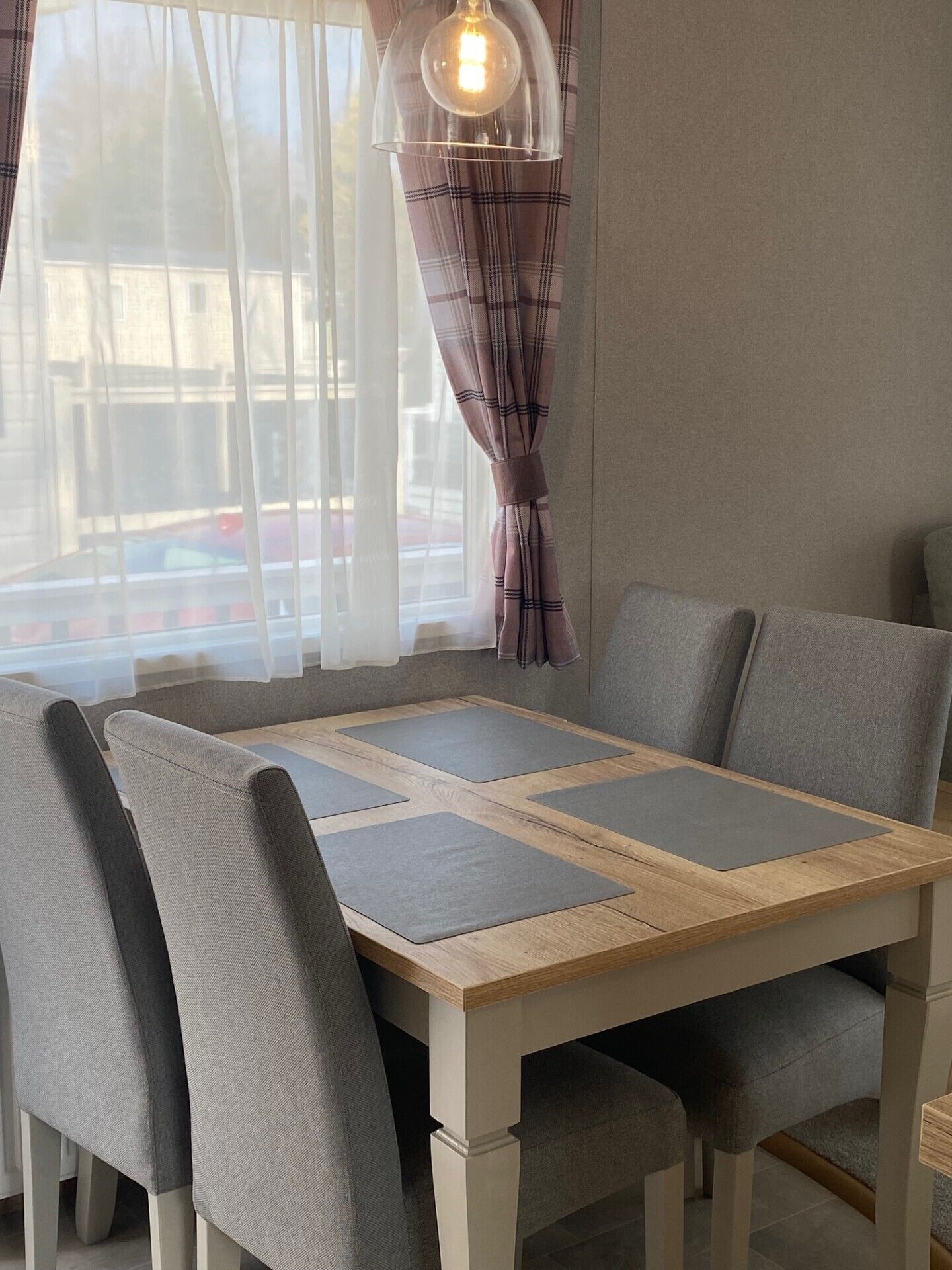 A dining area with a wooden table, grey upholstered chairs, and a pendant light.