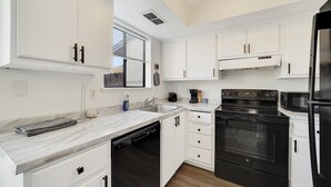 Una cocina con gabinetes blancos, una estufa negra, un microondas y un lavavajillas.