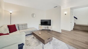 Una sala de estar moderna con sofá, mesa de centro, televisor y una escalera que sube a otro nivel.