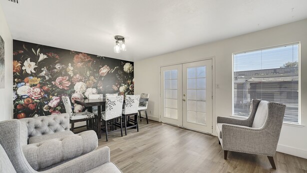 Amplia sala de estar con un sofá y un sillón de color gris, y un comedor con un fondo de papel tapiz floral.