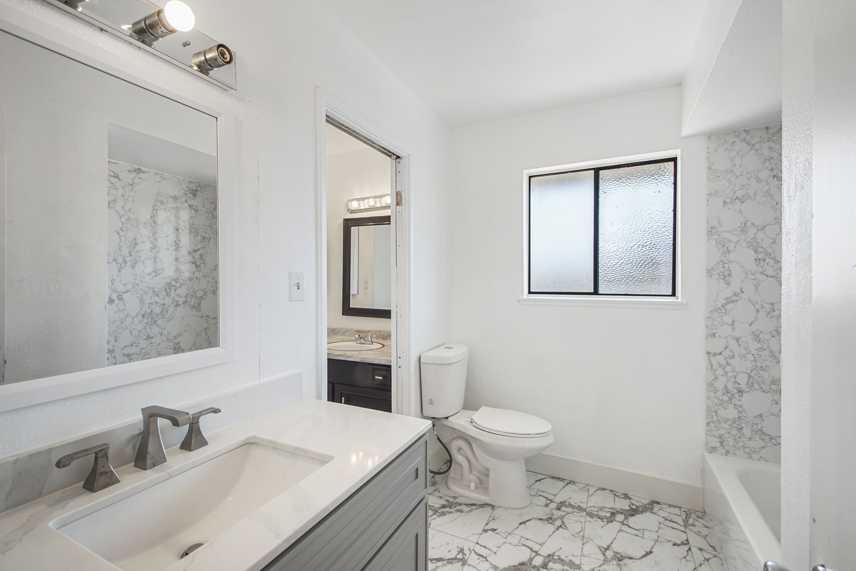 Een badkamer met een wit wastafel, twee kraan, een toilet en een spiegel met verlichting.