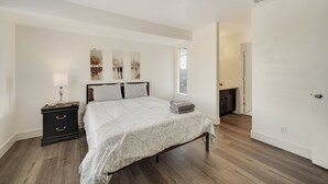 Un dormitorio con cama, mesita de noche, lámpara y una obra de arte en la pared.