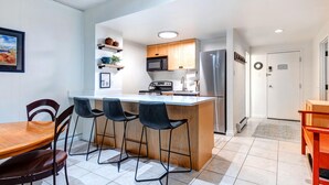 A modern kitchen with a central island, bar stools, a microwave, and a refrigerator.
