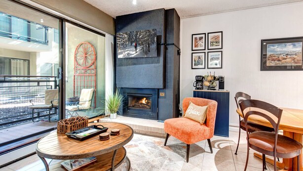 A modern living room with a fireplace, a round wooden table, and a seating area with a chair and a sofa.