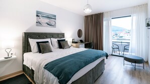 Habitación de hotel moderna con una cama grande, un escritorio, una silla y un balcón con vistas a la ciudad.