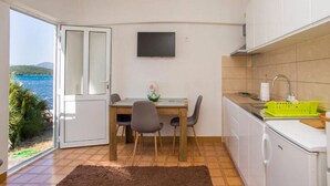 A compact kitchen with a dining area, a TV mounted on the wall, and a view of the sea through the door. - Apartment Pascal - One Bedroom Apartment with Terrace and Sea View (Janjina)