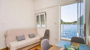 A small, cozy room with a sofa and a table, a window with a view of the water, and a door leading outside. - Apartment Pascal - One Bedroom Apartment with Terrace and Sea View (Janjina)
