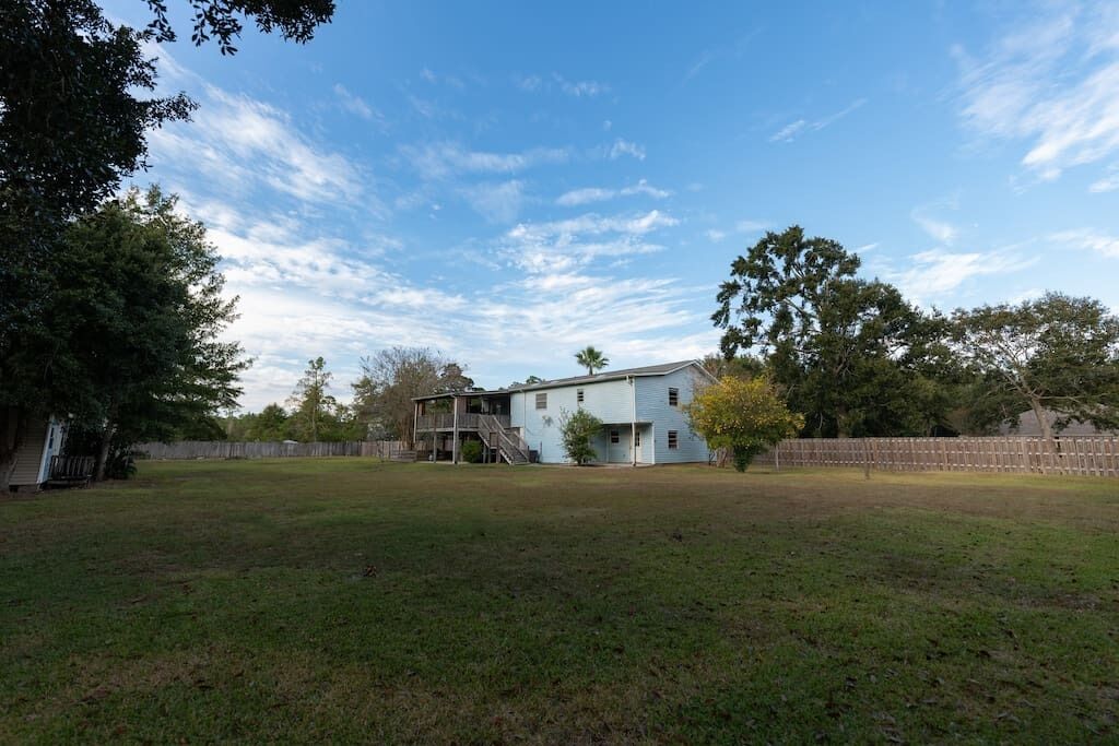A two-story house with a large backyard, a wooden deck, and a staircase leading to the upper floor.