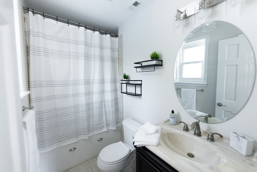 Een moderne badkamer met een gestreept douchegordijn, een toilet, een wastafel met spiegel en twee wandplanken met planten.