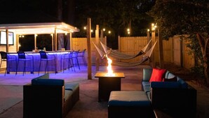 Un patio exterior con una hamaca, un pozo de fuego y una zona de bar con sillas y una mesa.