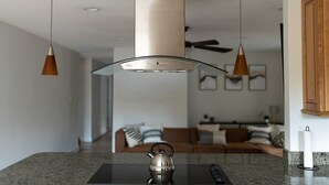 Una cocina moderna con una isla central, luces colgantes y un hervidor de acero inoxidable.