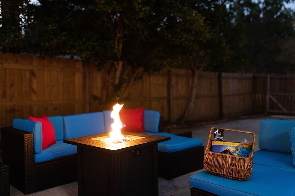 A patio area with a square table, blue cushioned seating, and a fire feature.