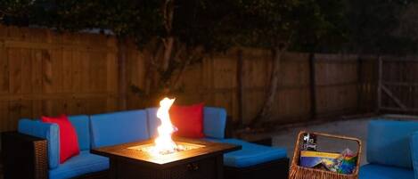 A patio area with a square table, blue cushioned seating, and a fire feature.