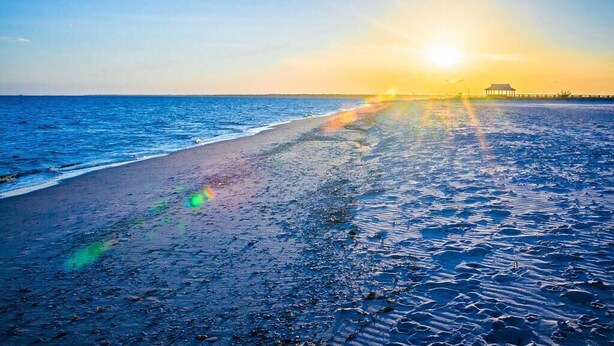Una playa con un muelle que se adentra en el agua, bajo un cielo despejado.