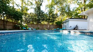 Una piscina limpia sin elementos acuáticos visibles, rodeada por una cerca de madera y un pequeño edificio con fachada blanca.