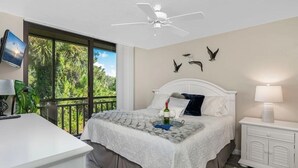 Una camera da letto con un letto, un comodino, una scrivania e un balcone con vista sugli alberi.