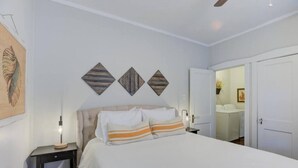 Ein Schlafzimmer mit einem Bett, Nachttischen, einem Deckenventilator und einer Tür zu einem Badezimmer.