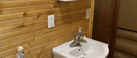 Un baño con paneles de madera, un inodoro, un lavabo con un espejo encima y una botella de jabón de manos sobre el inodoro.
