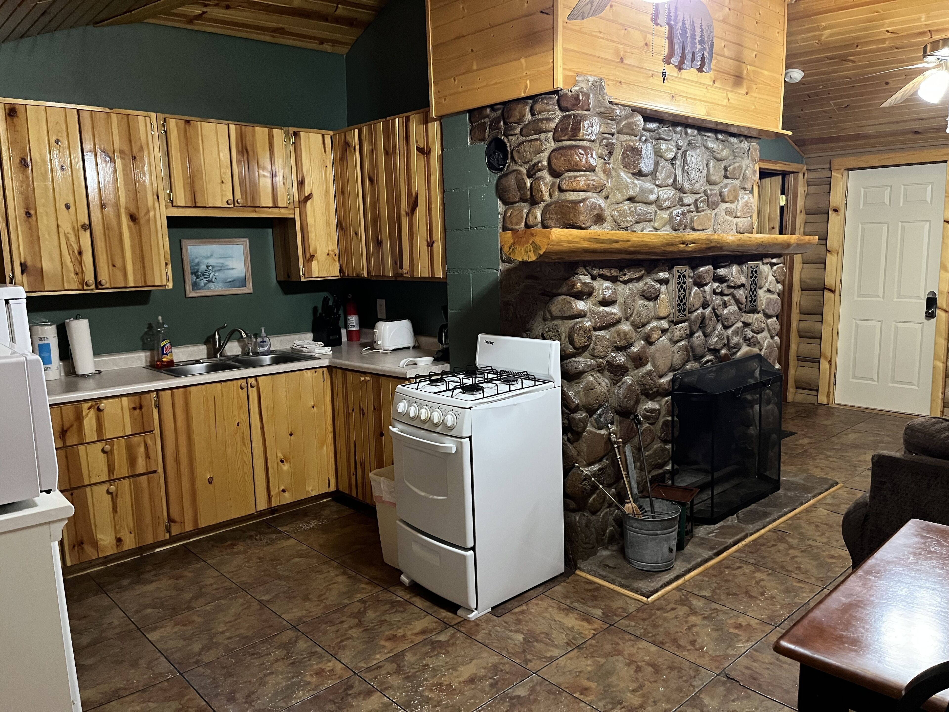 A kitchen with wooden cabinets, a stone fireplace, a gas stove, and a tiled floor.