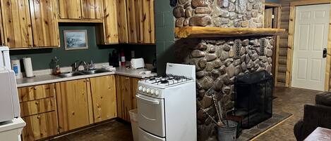 A kitchen with wooden cabinets, a stone fireplace, a gas stove, and a tiled floor.