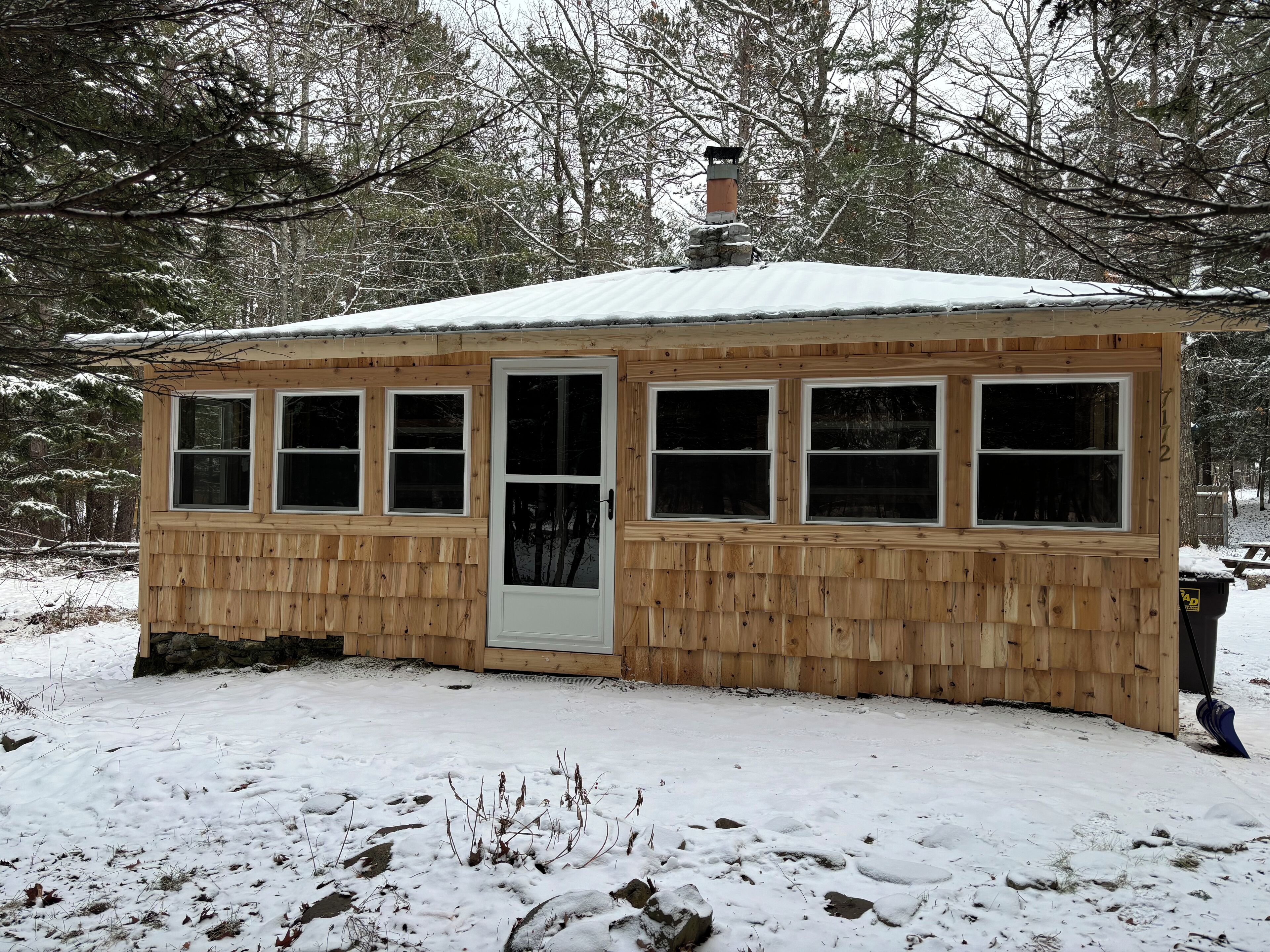 A small wooden cabin with a metal roof, a chimney, and multiple windows.