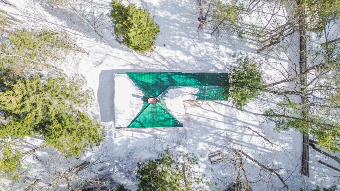 Vista aérea de una zona cubierta de nieve con una estructura verde distintiva, rodeada de árboles.