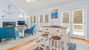 Een moderne woonkamer met een open haard, blauwe banken, een eethoek met krukken en grote ramen met zonwering.