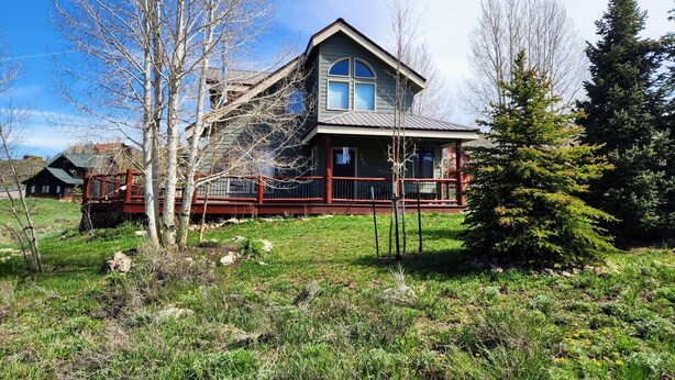 Una casa de dos pisos con un porche amplio, rodeada de césped y árboles.