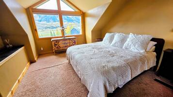 A bedroom with a large window, a bed, a dresser, and a lamp.