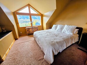 A bedroom with a large window, a bed, a dresser, and a lamp. - CB South Home | 3 Bedroom | Deck Views | Grill | Parking (Crested Butte)