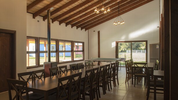 A spacious dining area with high ceilings and large windows, featuring multiple tables and chairs.
