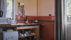 A compact kitchen with a microwave, stove, sink, and wooden shelves.