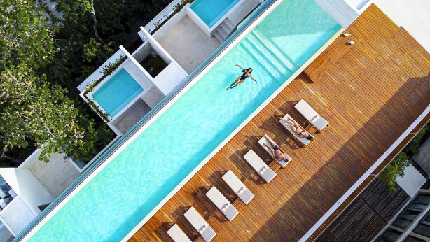 An aerial view of a swimming pool with multiple lanes, surrounded by lounge chairs and a wooden deck. - Vita Tulum (Tulum)