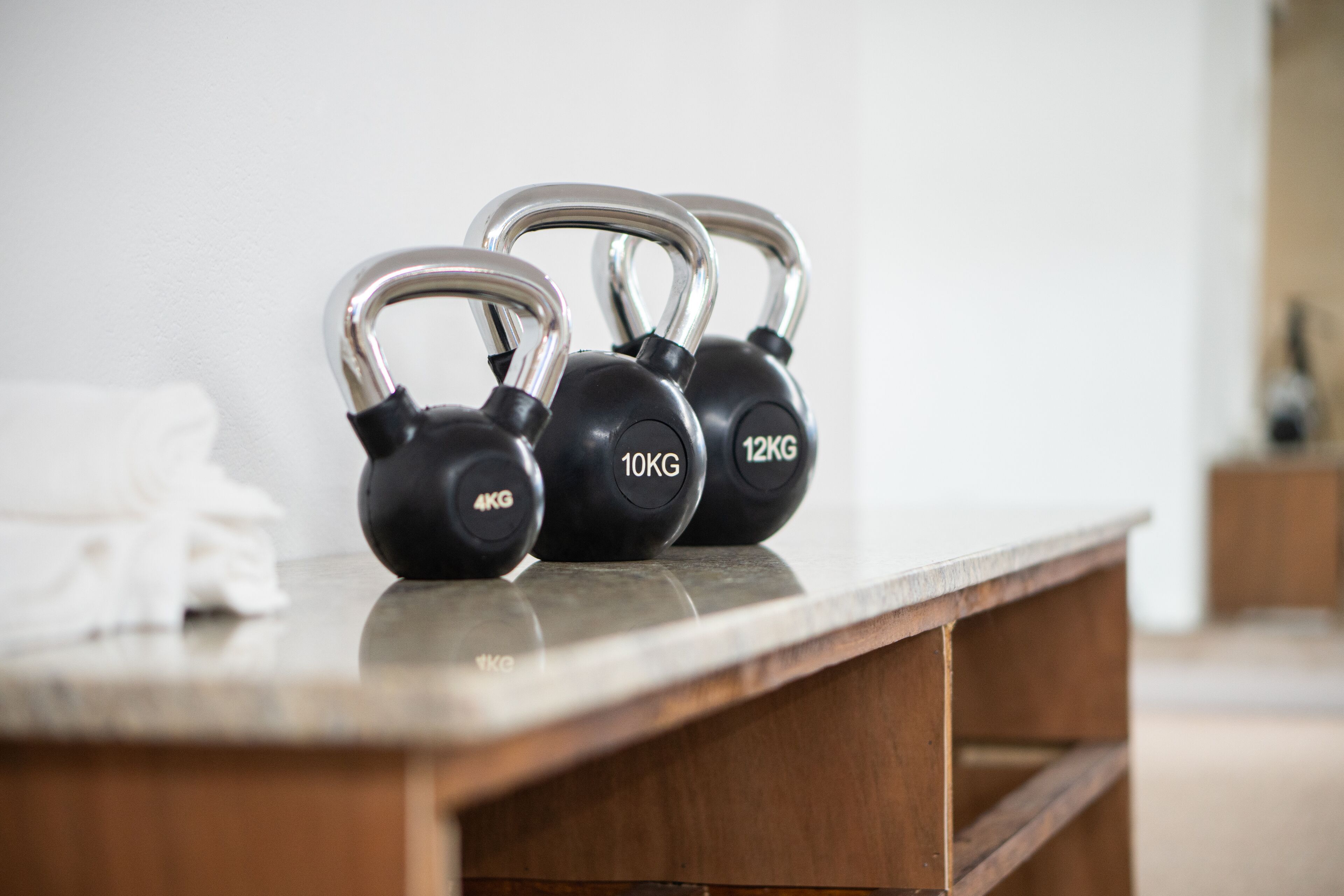 A set of kettlebells on a wooden table with weights labeled 4KG, 10KG, and 12KG.