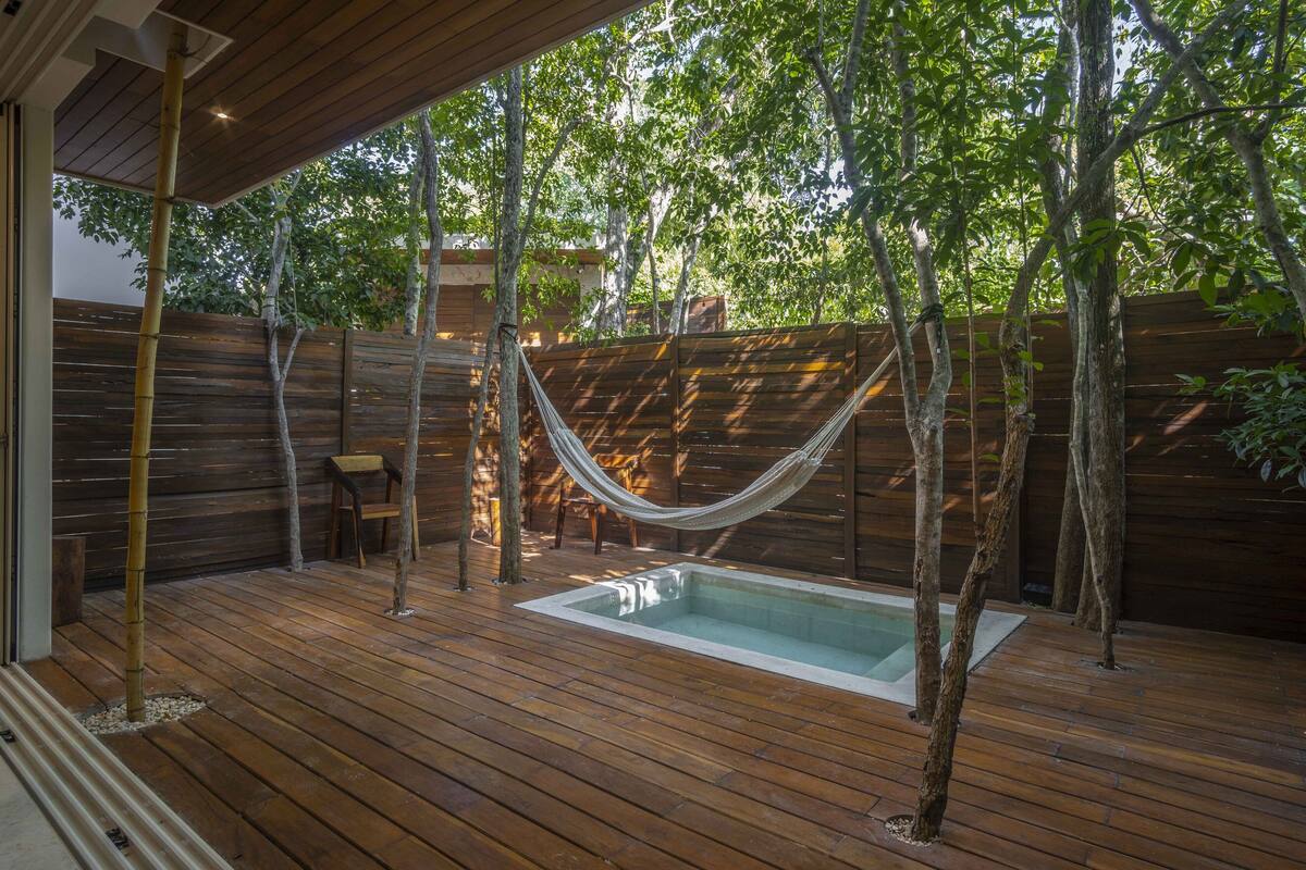 Terraza de madera con piscina, rodeada de árboles y una valla de madera.