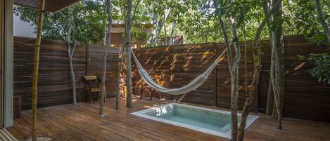 Une terrasse en bois avec une piscine, entourée d’arbres et d’une clôture en bois.