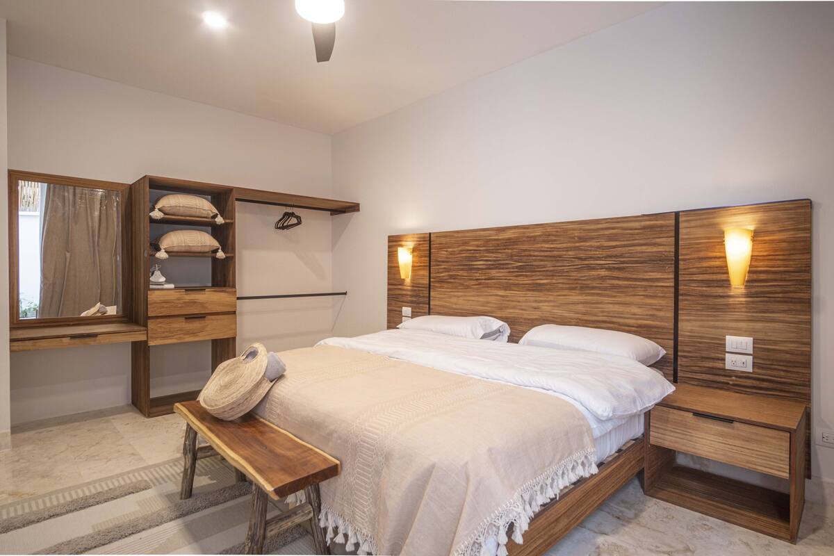 Un dormitorio moderno con cabecera de madera, una mesita de noche, un banco y un armario empotrado con estantes.