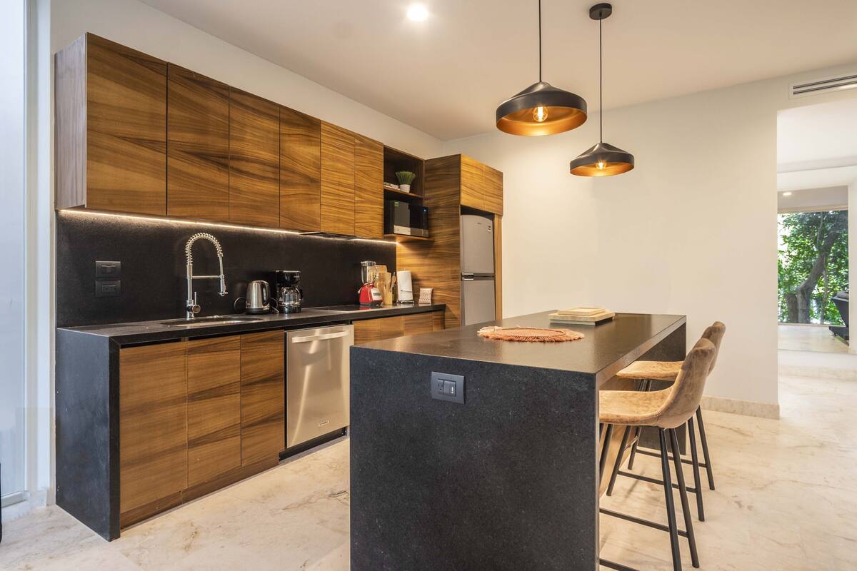 Una cocina moderna con armarios de madera, una isla central, taburetes de bar e iluminación colgante.